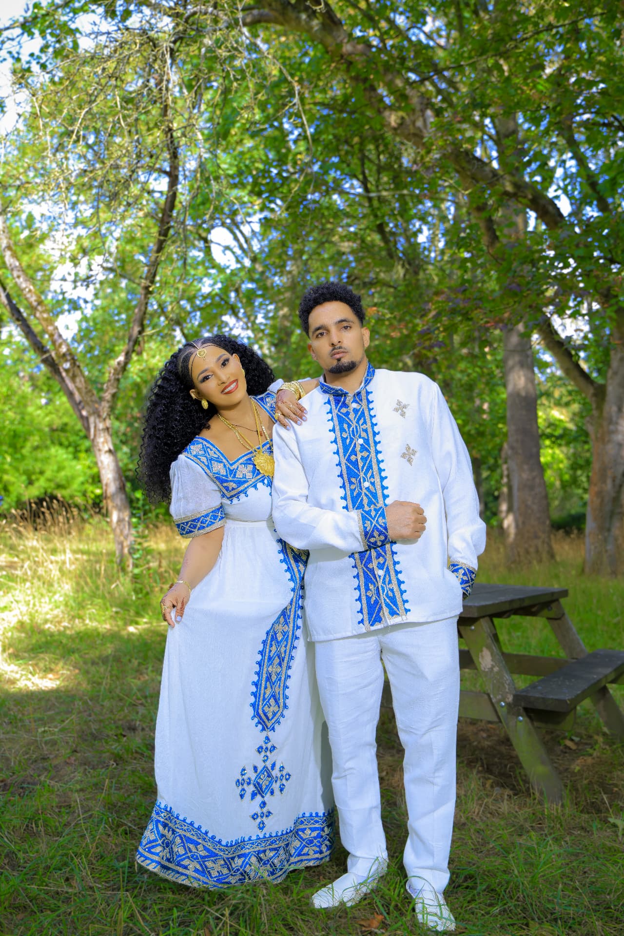 Couple in traditional white and blue Habesha wedding dress standing in a sunlit park