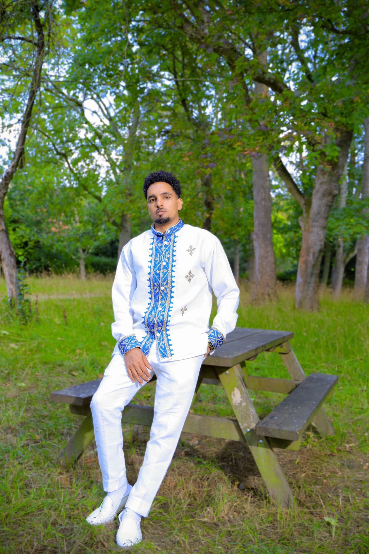 Groom in a white embroidered suit sitting on a picnic bench
