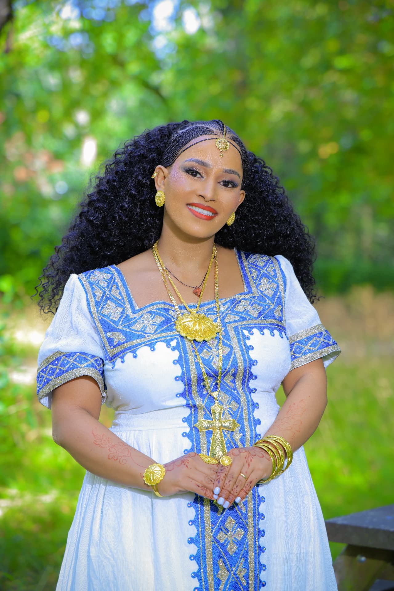 Bride smiling in a white and blue embroidered dress with gold jewellery